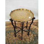 A brass tea tray table with scalloped edging, engraved in a Japanese theme, supported on a 6 arm/leg