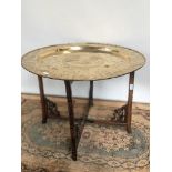 A 19th century gilt brass tea table, engraved with Chinese story sections, upon a hand carved