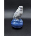 A Royal Copenhagen figurine Budgie sat on a piece of fruit. [14cm in height]