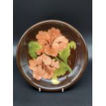 A Moorcroft Pink Hibiscus pattern plate. Designed with a brown ground. [22cm in diameter]