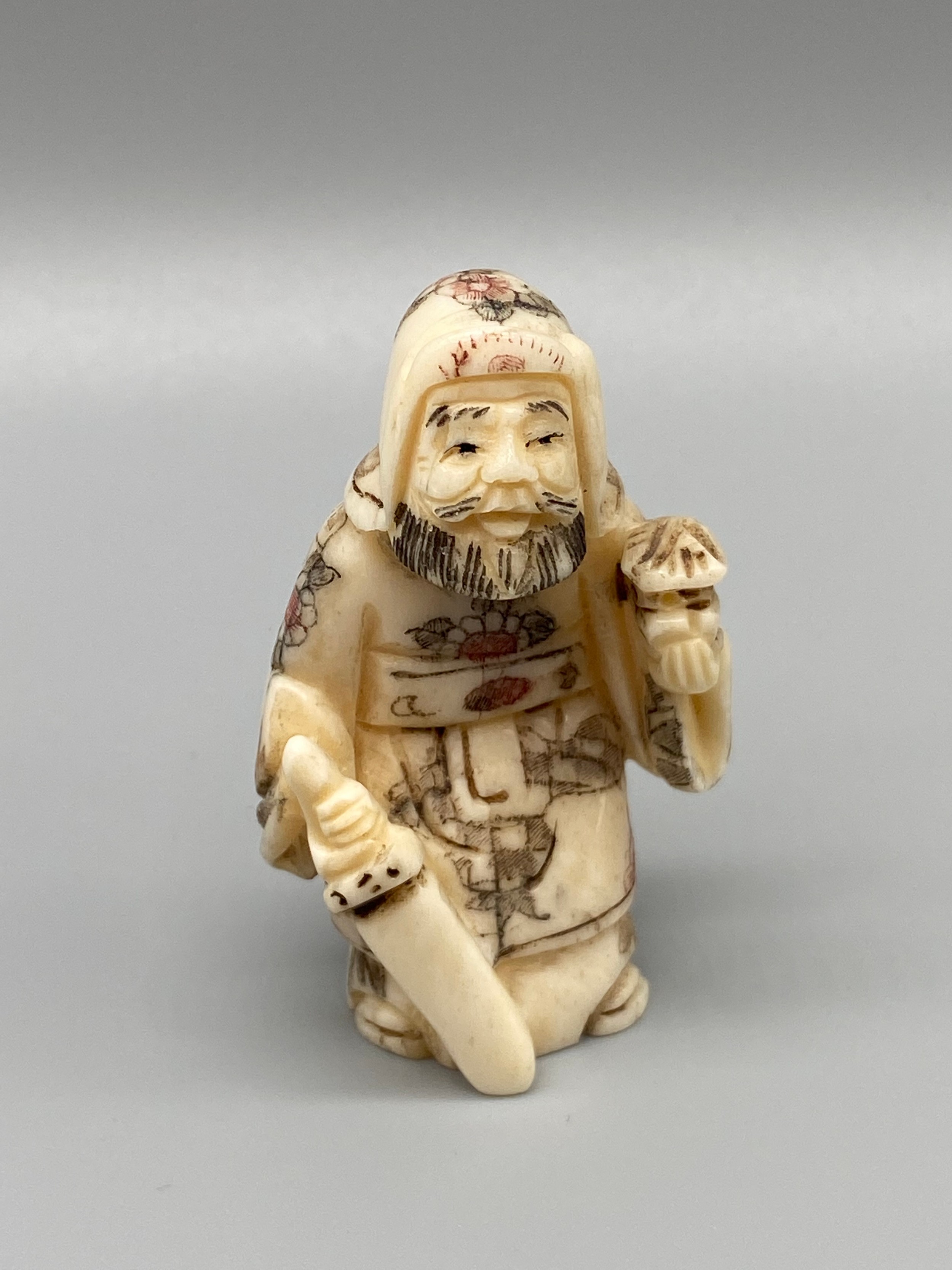 An early 20th century Japanese hand carved bone netsuke of a cloaked gentleman holding a sword and