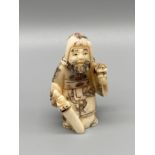 An early 20th century Japanese hand carved bone netsuke of a cloaked gentleman holding a sword and