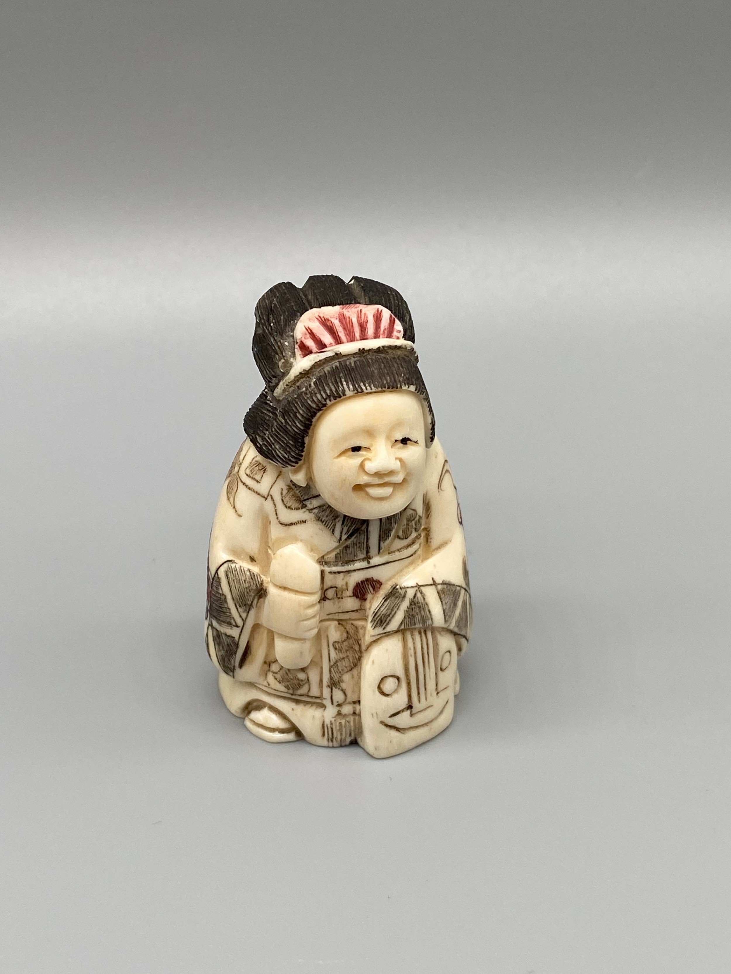 A Japanese hand carved bone netsuke of a women in an ornate robe. Signed. [5cm in height]