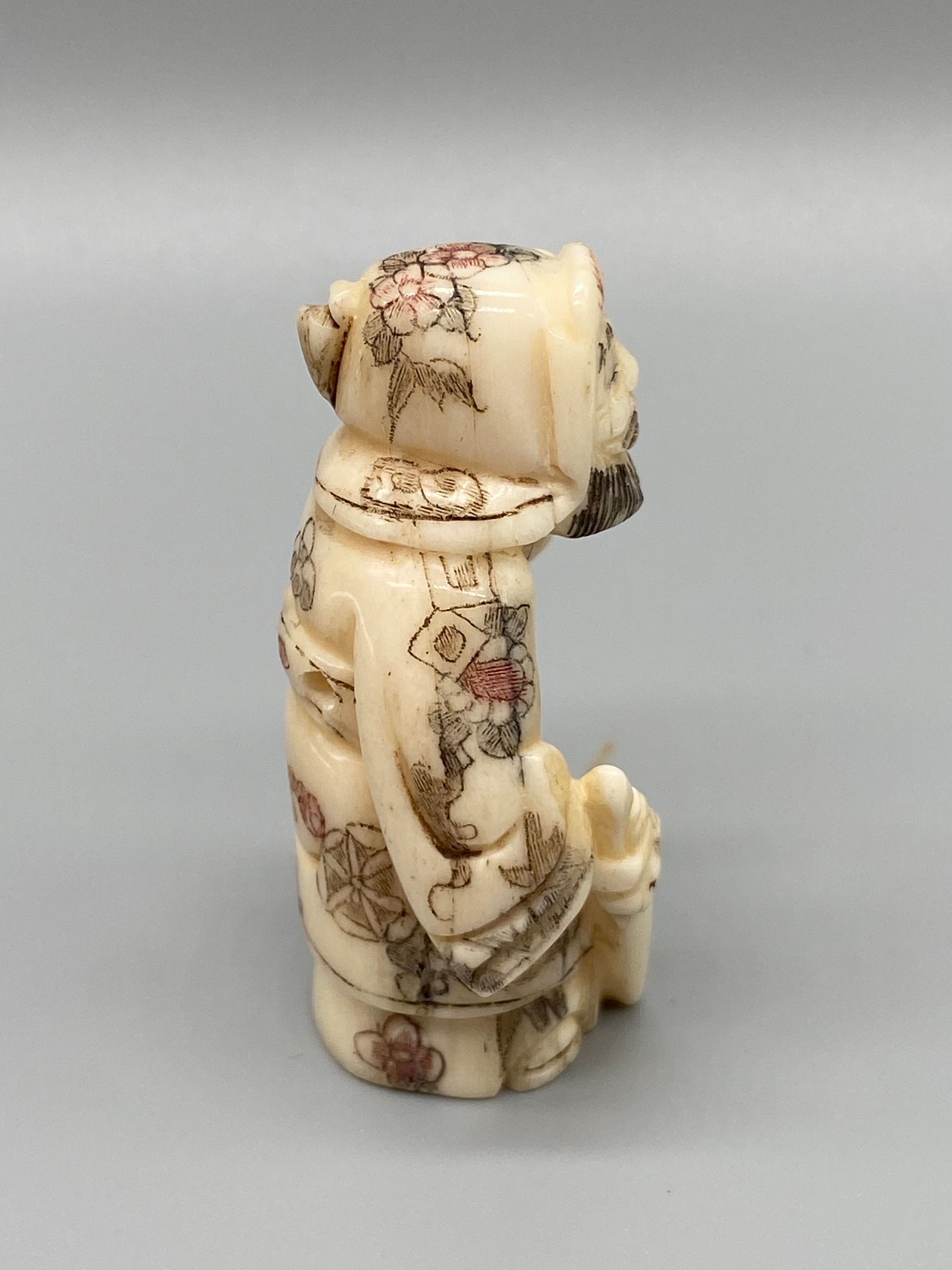 An early 20th century Japanese hand carved bone netsuke of a cloaked gentleman holding a sword and - Image 2 of 5