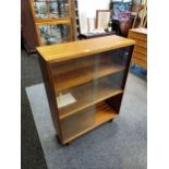 A mid century teak two tier bookcase. designed with glass sliding doors and on pedestal legs. [