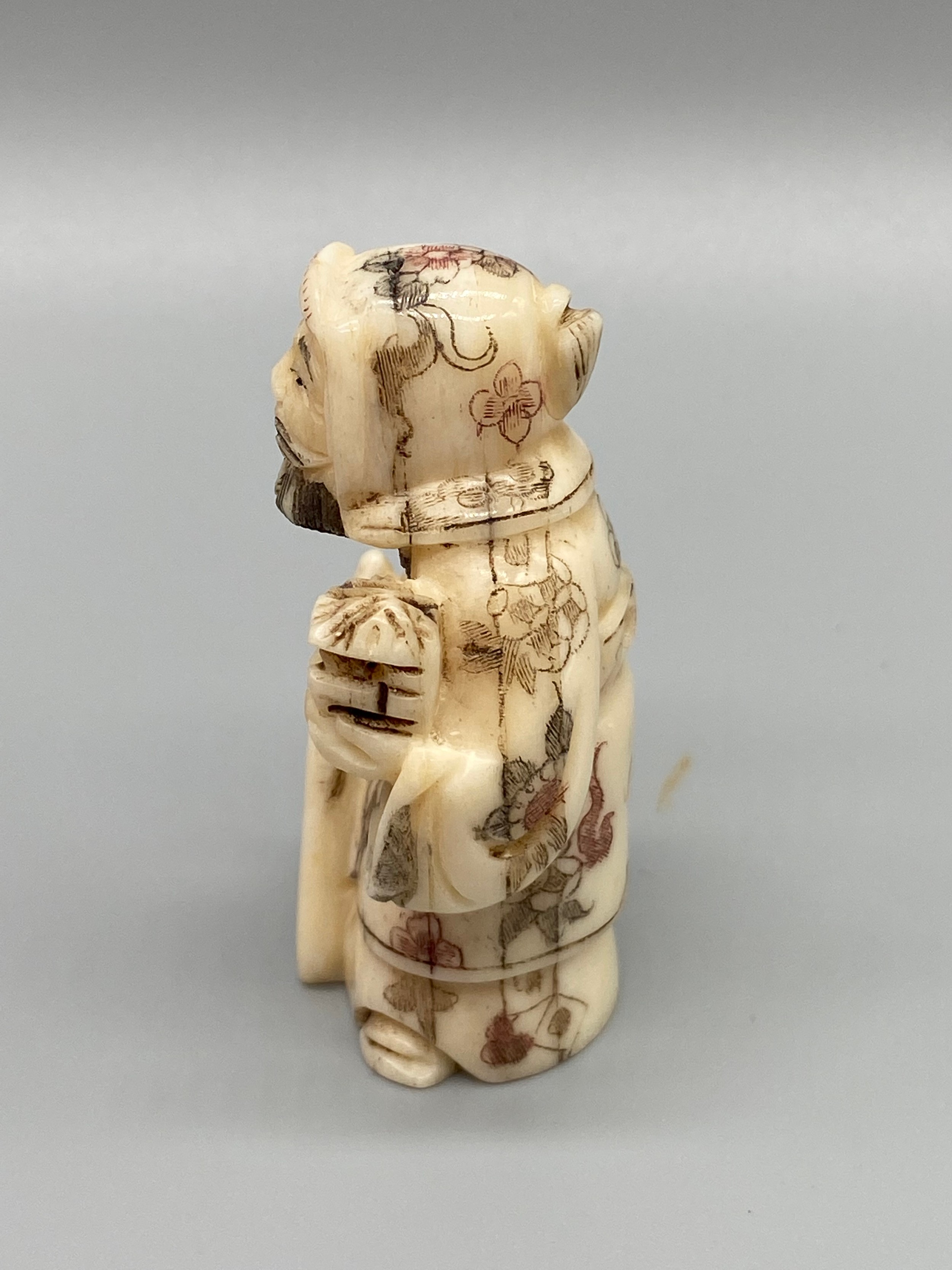 An early 20th century Japanese hand carved bone netsuke of a cloaked gentleman holding a sword and - Image 3 of 5