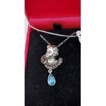 A silver pendant necklace of a figure with pear shaped blue topaz drop
