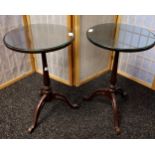 Matching pair of mahogany lamp tables, circular top with glass insert, supported on a tripod base [