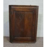 A small provincial George III oak and elm corner cabinet, with a panelled door, opening to reveal