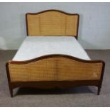 A caned and hardwood framed bedstead, 20th century, with a high and serpentine bead head and