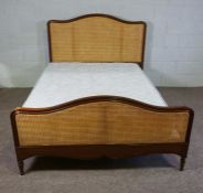 A caned and hardwood framed bedstead, 20th century, with a high and serpentine bead head and