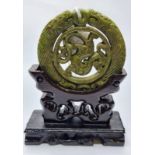 A Chinese carved green jade disc (amulet?) with mythical beasts on a custom made wooden base. Disc
