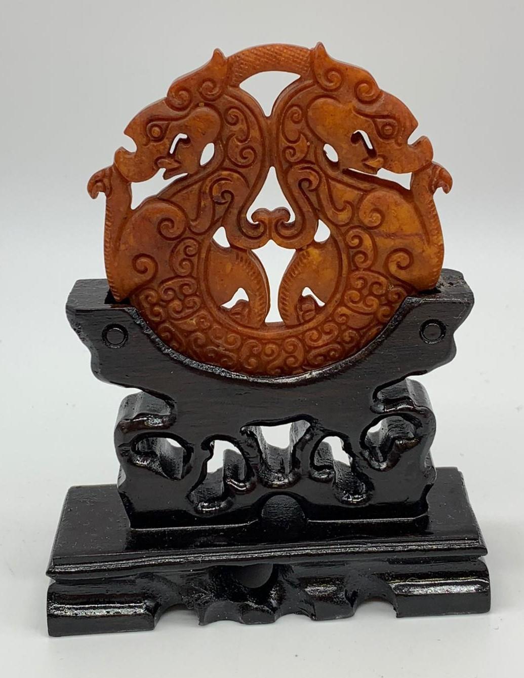 A Chinese, hand carved on both sides and pierced, orange hard stone amulet representing two