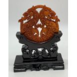 A Chinese, hand carved on both sides and pierced, orange hard stone amulet representing two