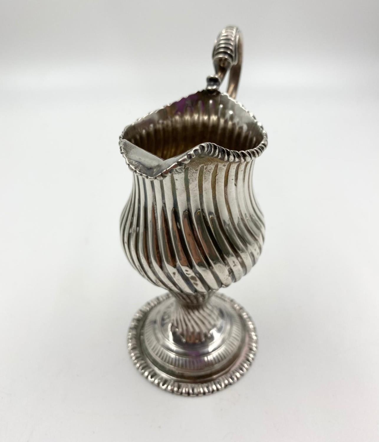 A finely detailed silver creamer in ribbed swirl pattern with curved handle on a pedestal base. 14cm - Image 2 of 4