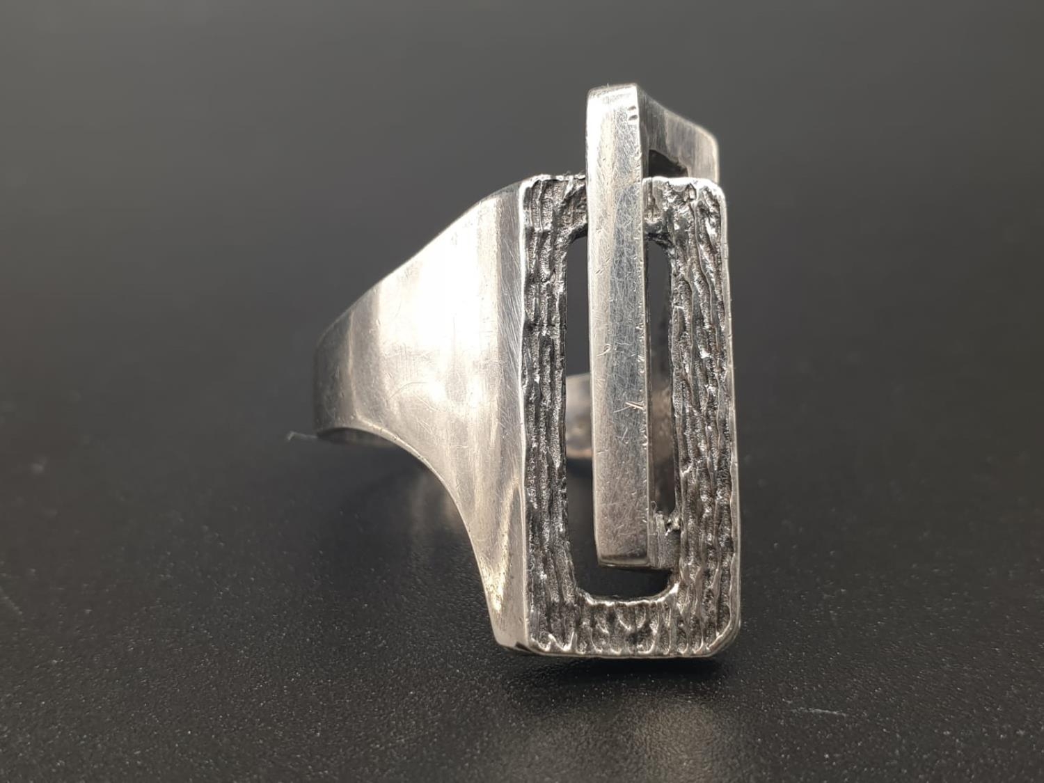 AN UNUSUAL SHAPED SILVER DRESS RING WITH TWO RECTANGULAR SHAPES INTERLOCKED. 8.6gms size N/M