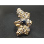 A naturalistic silver and gold ring in the shape of an ivy leaf. A central faceted Ceylon sapphire