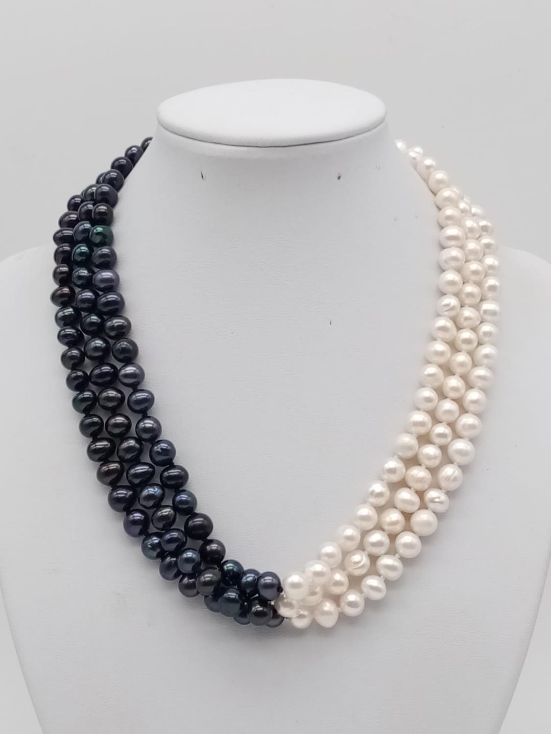 A glamourous, three rows of black and white pearls necklace with a flower shaped, hand carved,