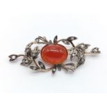 An antique brooch with a central oval carnelian surrounded by diamonds set in a floral design.