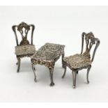 A HALL MARKED SILVER MINIATURE TABLE AND 2 CHAIR SET MADE BY A CHICK AND SONS. 34.3gms table