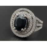 A vey attractive 14K white gold ring with a central oval faceted sapphire surrounded by 83 brilliant