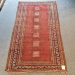 A red ground Persian rug, main blue border, centre with repeating square medallions, 175 x 100 cm