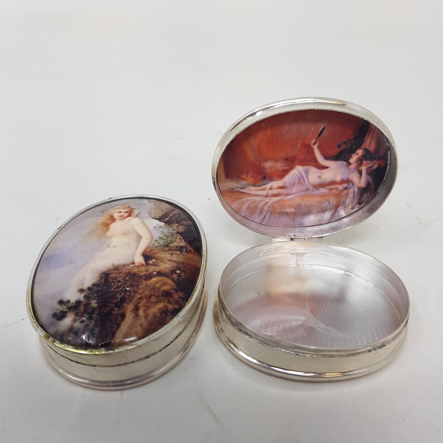 A modern silver coloured metal enamel oval pill box, decorated with fairy, 6 cm wide, and another,