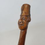 A folk art walking stick, the carved handle in the form of a smiling soldier with a bearskin type