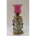 An oil lamp, with cranberry glass shade, with porcelain body, with floral handles, decorated birds