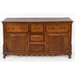 An oak dresser base, crossbanded in mahogany, having an arrangement of five drawers and a pair of