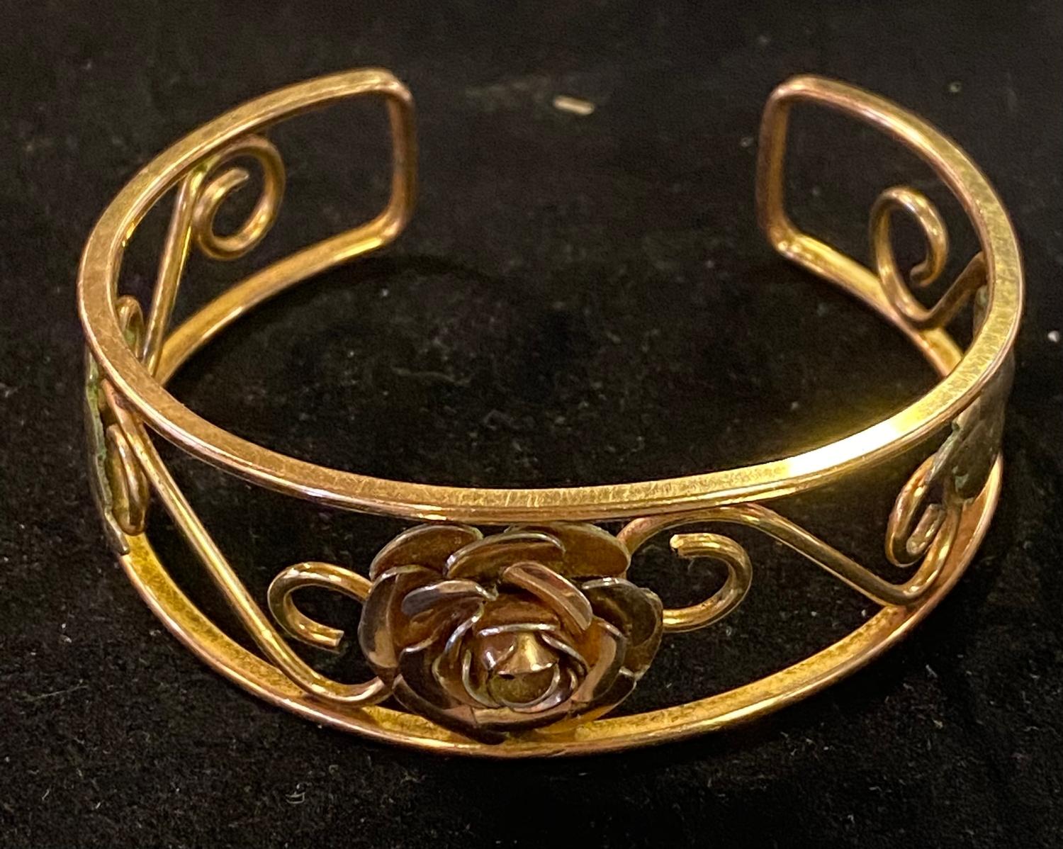 A two colour yellow coloured metal bangle, decorated a flowerhead, scrolls and leaves, 6.5 cm wide