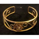 A two colour yellow coloured metal bangle, decorated a flowerhead, scrolls and leaves, 6.5 cm wide