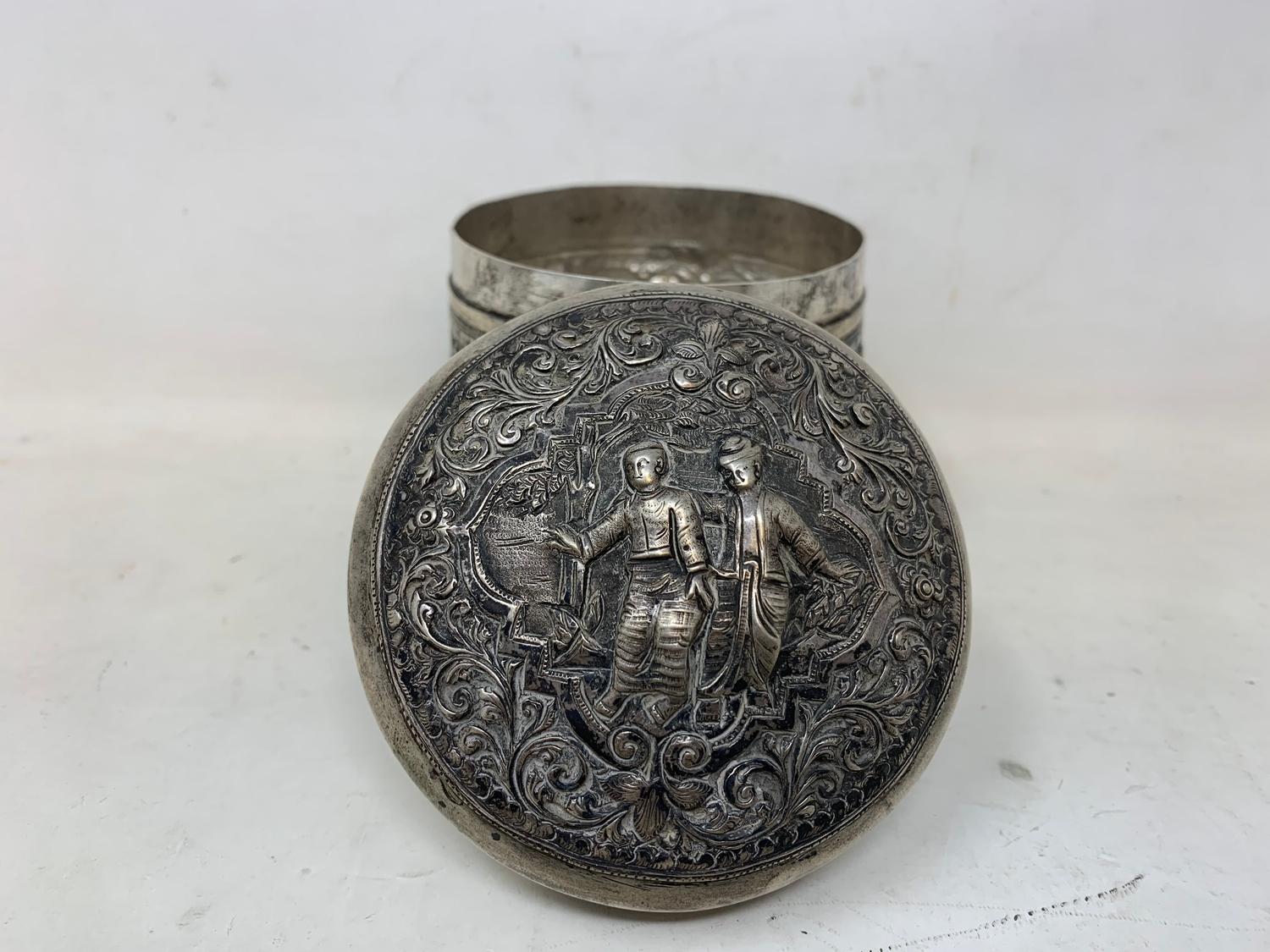 A Burmese silver coloured metal cylindrical box and cover, embossed figures, the base engraved a - Image 2 of 8