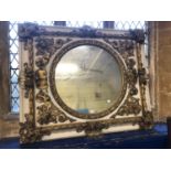 A mirror, the circular plate in a frame applied giltwood carvings with face masks, shells and