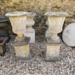 A pair of composition stone garden urns, raised on rectangular plinths, 92 cm high (2)