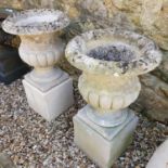 A pair of composition stone campagna form garden urns, raised on rectangular plinths, 86 cm high