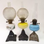 A cast metal oil lamp, with a yellow glass well, 59 cm high, and two other oil lamps (3)