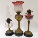 A brass oil lamp, with a cranberry lamp shade, 74 cm high, and two other oil lamps (3)