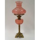 An early 20th century brass oil lamp, with cranberry shade and well, 67 cm high Converted to