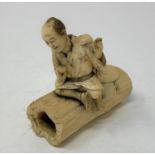 A Japanese carved ivory figure, of a man sitting on a hollow tree trunk section, lacks right hand,