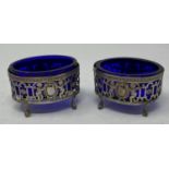 A pair of Dutch silver coloured metal oval salts decorated cherubs, with blue glass liners, 7.5 cm