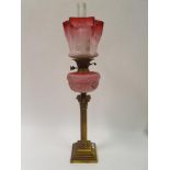 A brass oil lamp, with a ruby glass shade, pink glass well, base in the form of a corinthian column,