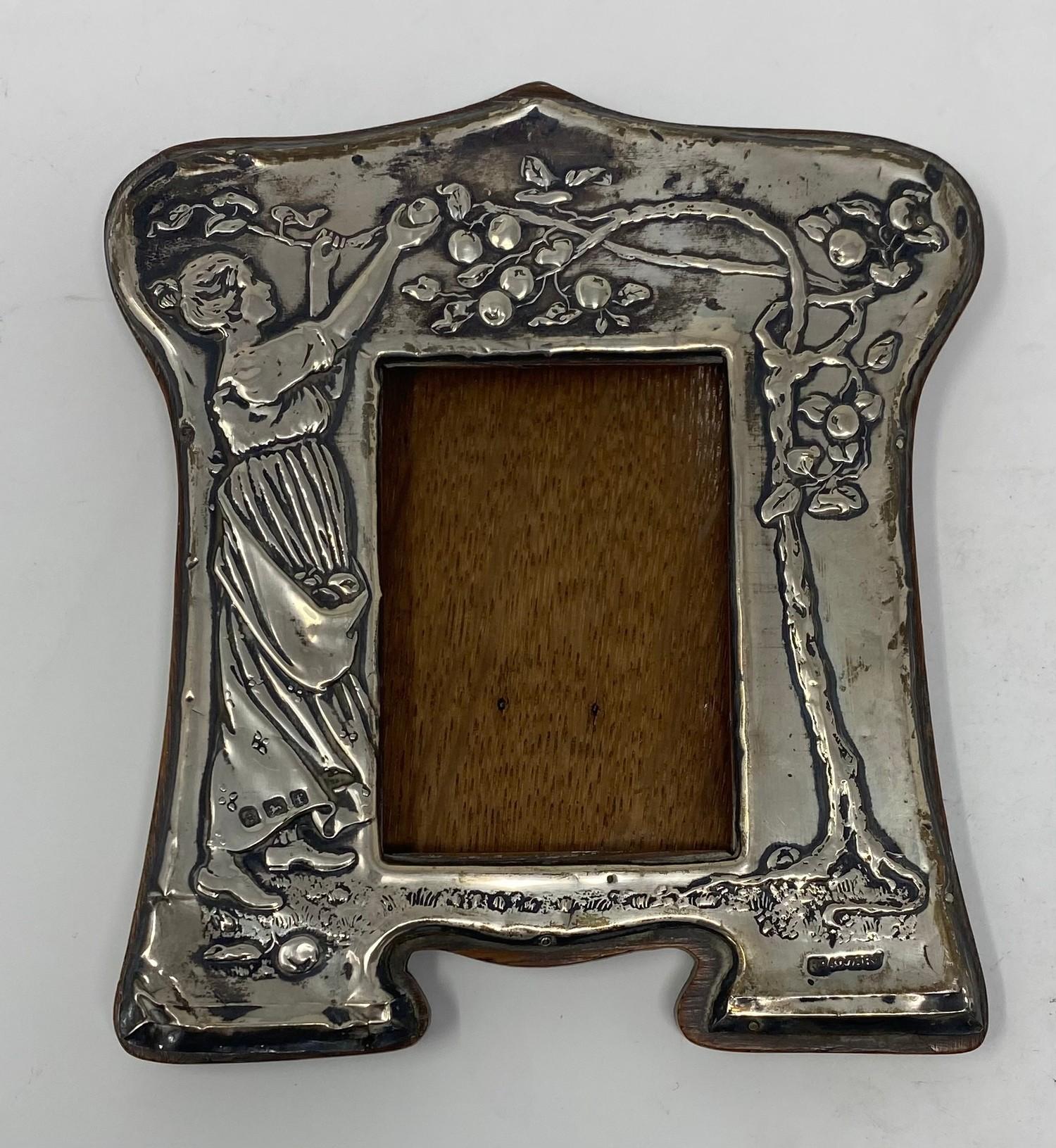 An early 20th century silver mounted strut photograph frame, embossed a lady picking apples,