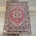 A Persian red ground rug, main cream border, centre with stepped medallions and stylised bird forms,