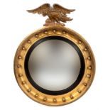 A carved giltwood convex wall mirror, with eagle finial 66 cm diameter Lacking one of the balls, and