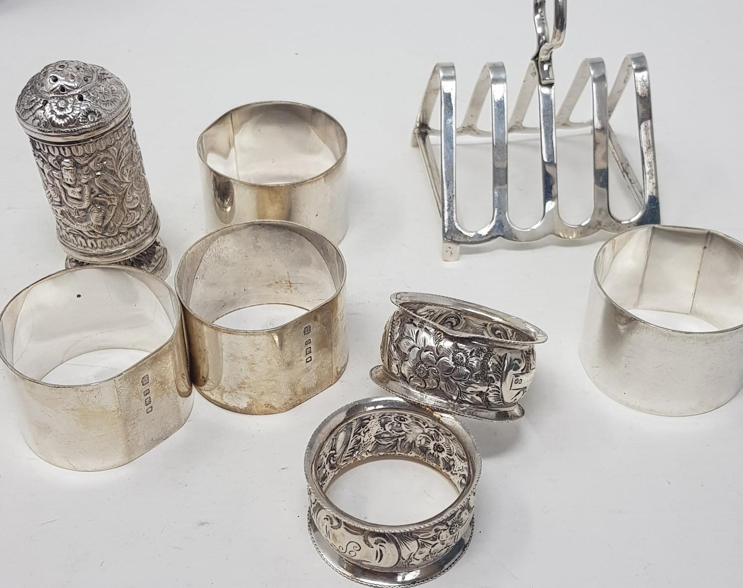 A silver toast rack, six silver napkin rings and an Indian silver coloured metal pepper pot, 9.5 ozt