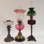 An oil lamp, with a cranberry glass shade, 63 cm high, another with a cranberry glass shade, 50 cm