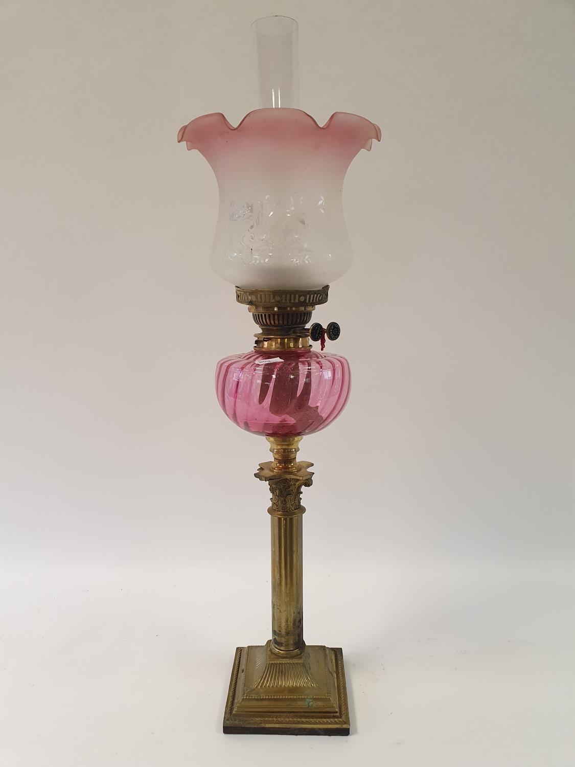 An oil lamp, with a cranberry tinted acid etched glass shade, a cranberry glass well, on a brass