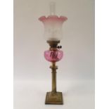 An oil lamp, with a cranberry tinted acid etched glass shade, a cranberry glass well, on a brass