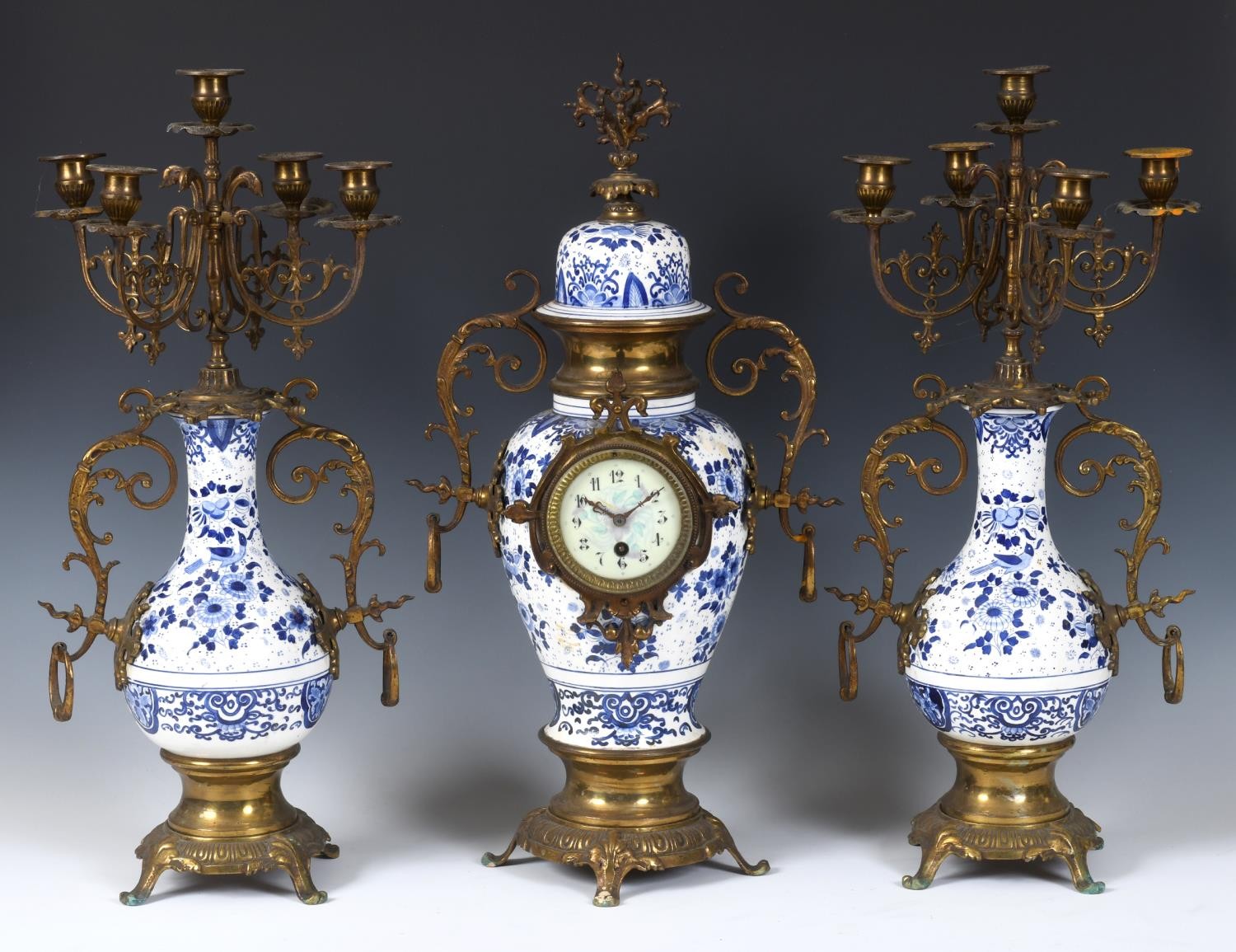 A clock garniture, the 8 cm diameter dial with Arabic numerals, in a pottery and gilt metal